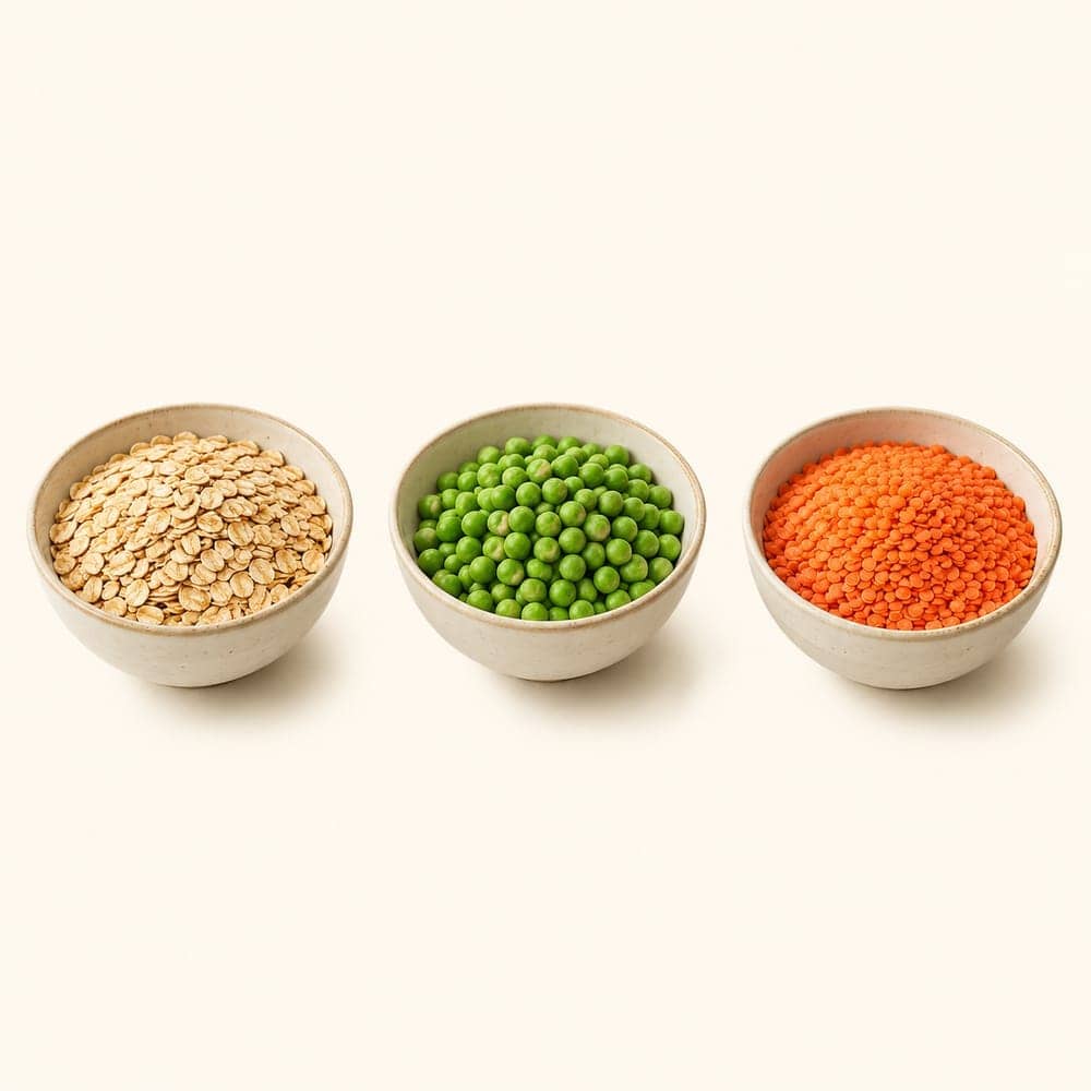 Bowls of oats, green peas and red lentils arranged on a seamless warm cream background.