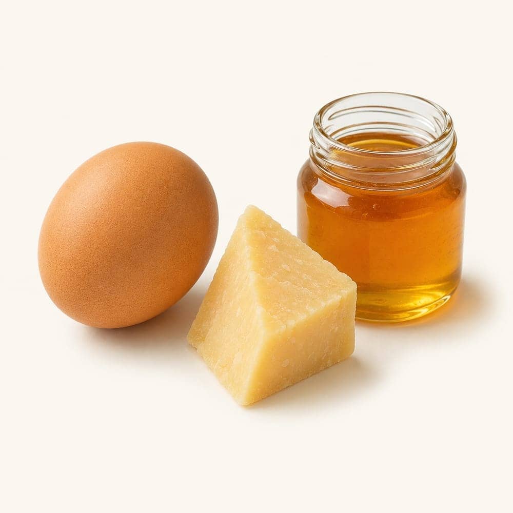 A single egg, a cheese wedge and a small honey jar arranged on a seamless warm cream background.